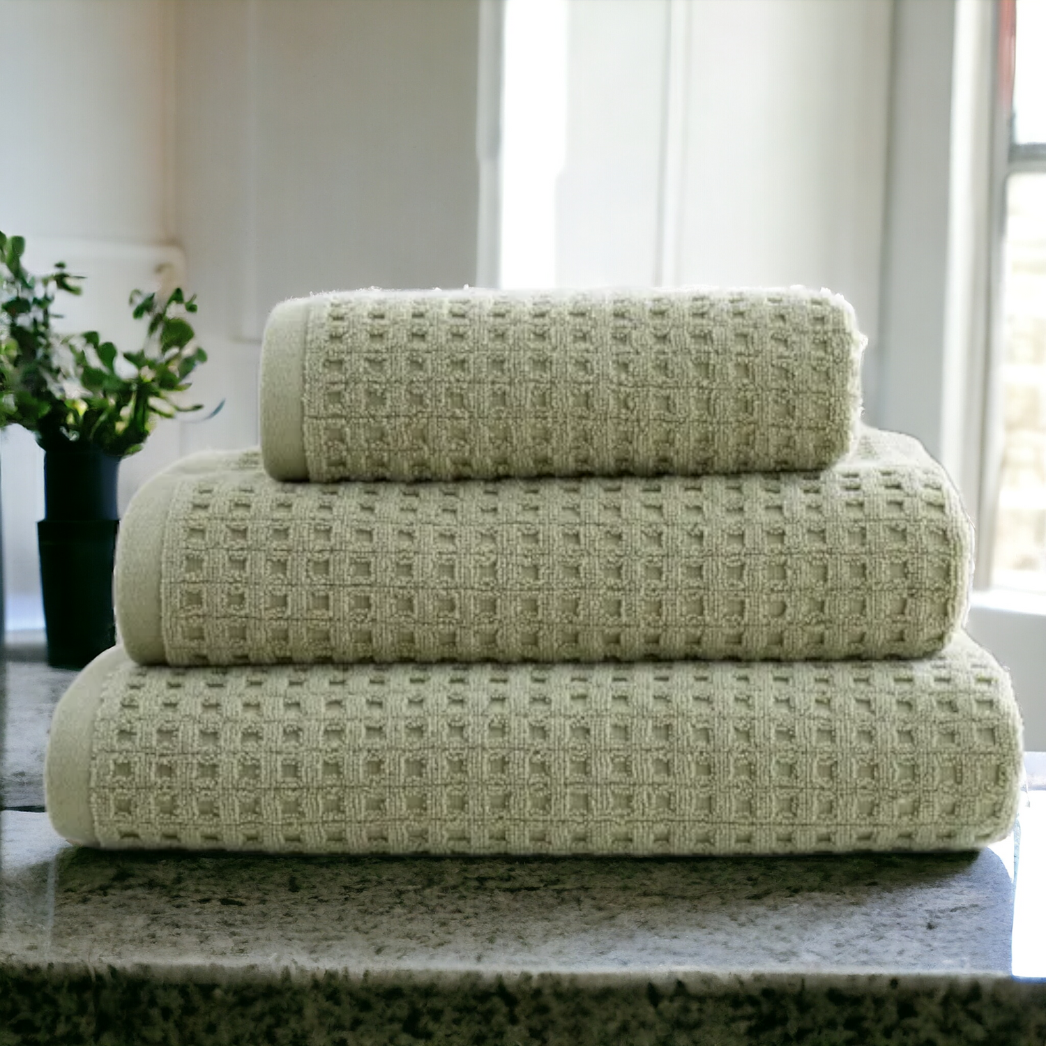 Stack of neatly folded towels on a counter with a decorative plant in the background, creating a serene and organized bathroom ambiance.