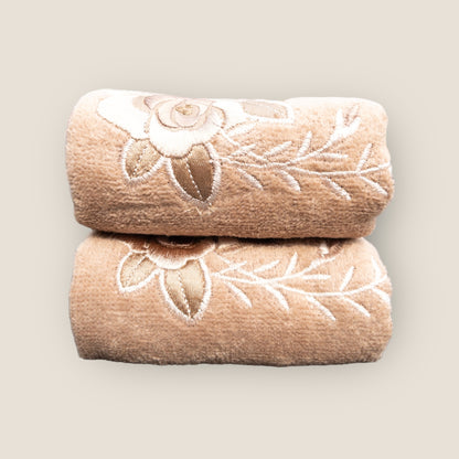 Two beige folded hand towels with big embroidered flowers made on it, stacked