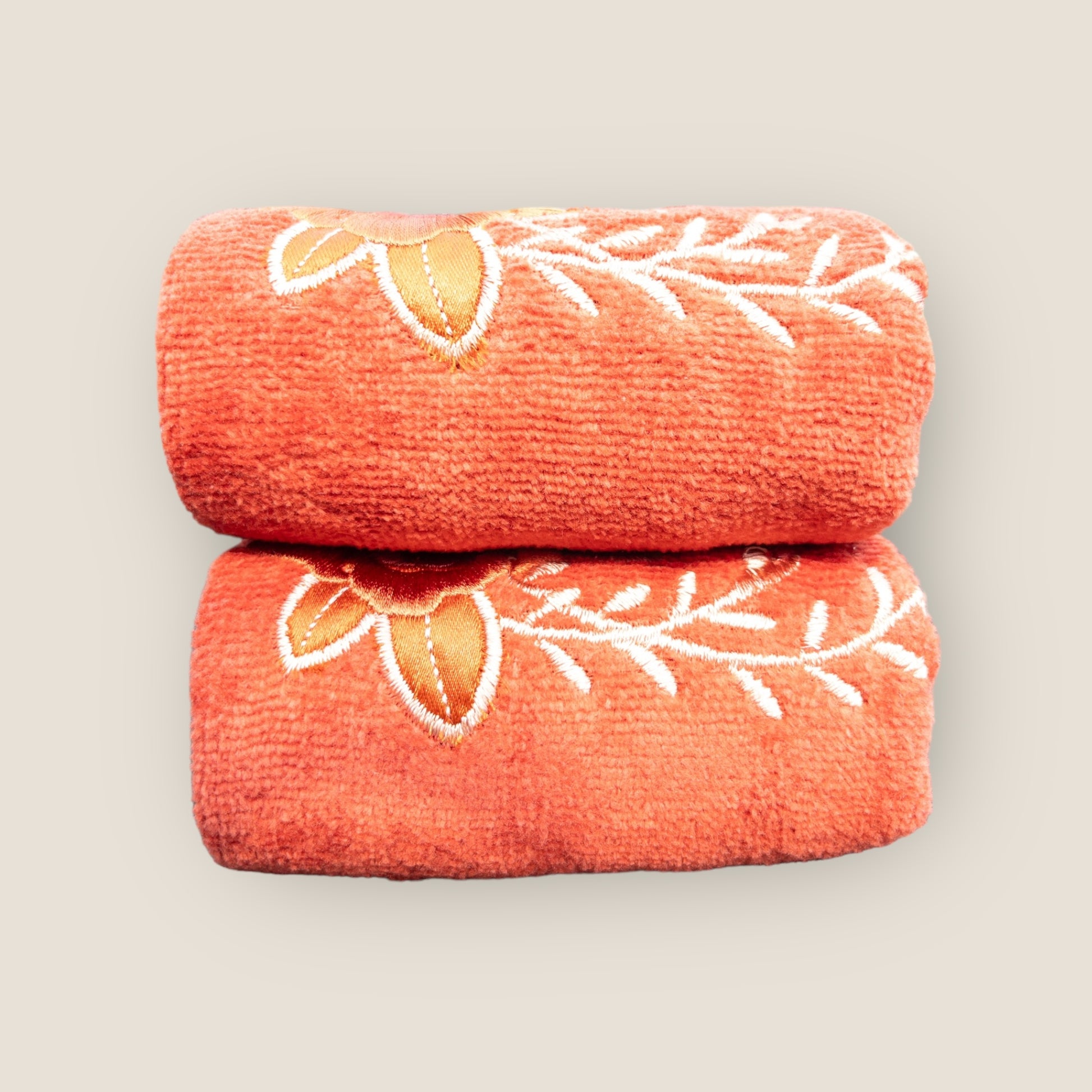 Two orange folded hand towels with big embroidered flowers made on it, stacked