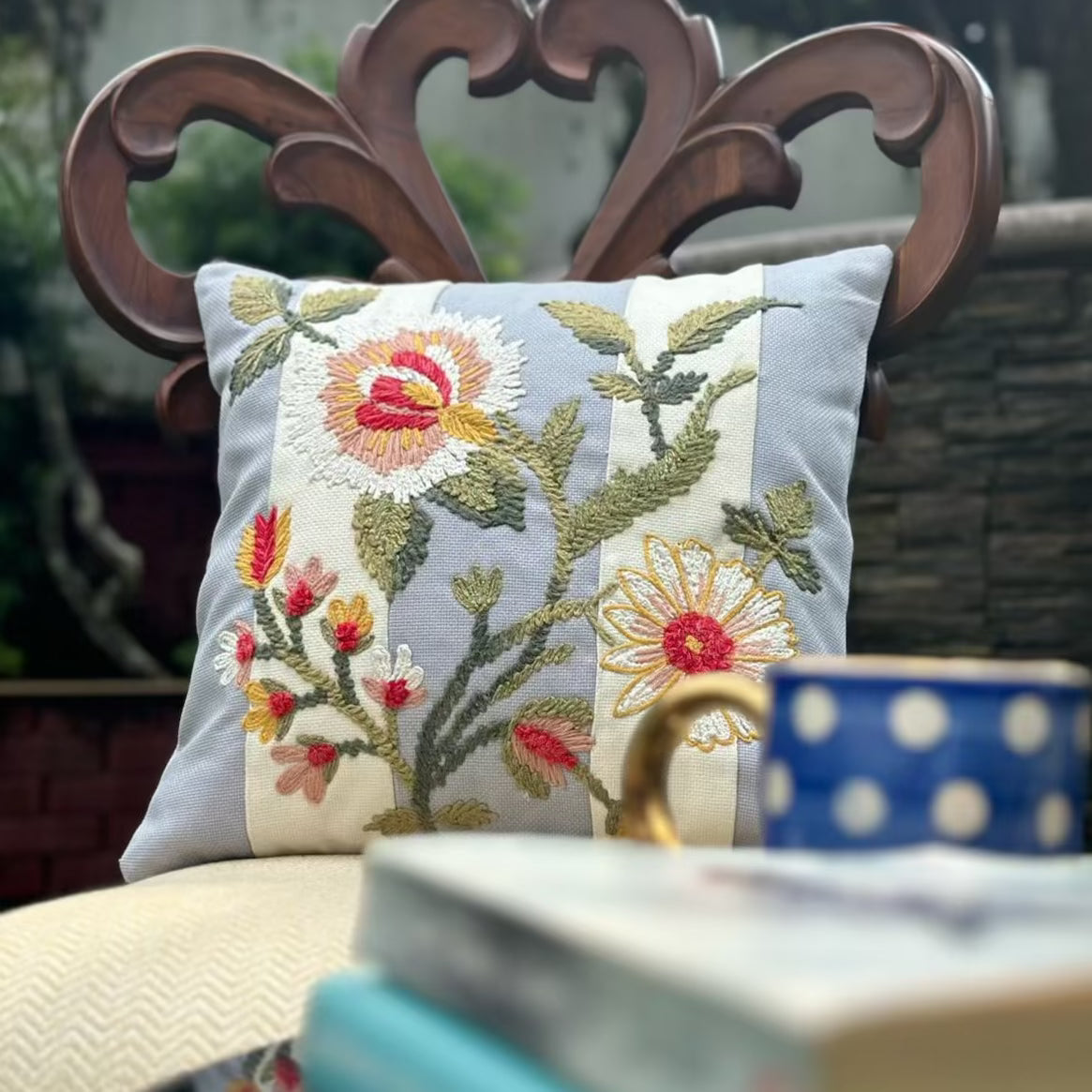 blue cushion cover with floral work and 2 white thick stripes, placed on a wooden chair