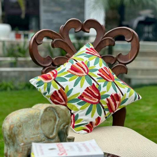 white cushion cover with red and green floral threadwork, placed on a wooden chair in a garden