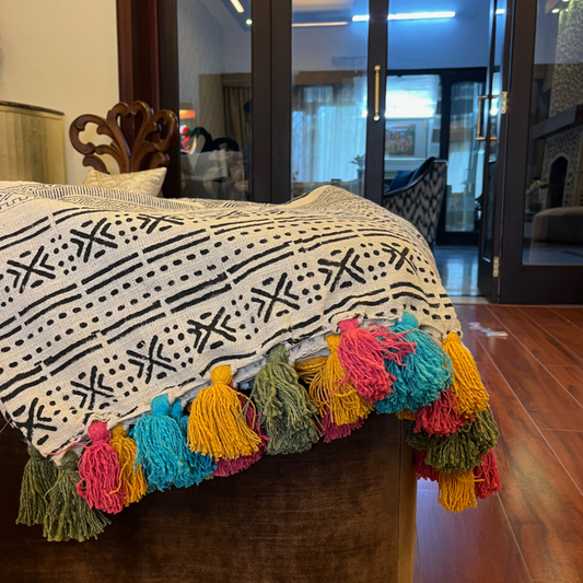 a black and white throw with multi color tassles styled on a pouf
